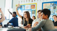 High school class with students raising hands. 