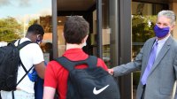 Principal greeting high school students in front of school.
