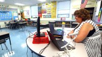 Teacher instructing students remotely sitting at her desk in her classroom