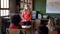 Teacher in a face mask instructs students from the front of her class
