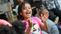 First-grade girl claps happily while sitting on the floor during class