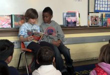 Two primary students are reading in front of the classroom