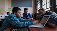 Teacher is helping the students work on the computer in a classroom.