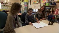 Two teachers are working with a student in a classroom