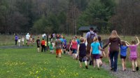 Group of teacehrs and students are on a field trip. They're walking in a green field.