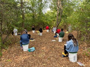 Students sitting on plastic buckets in outdoor classroom at Marshwood Great Works School