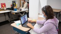 Student works on laptop in classroom while wearing mask