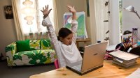 Elementary aged girl remote learning at home on computer and stretching at her desk 
