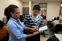 Female teacher uses iPad in classroom while male student participates