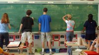 High school students writing Spanish words on chalk board in school. 