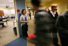 A high school teacher greets students as they enter her classroom