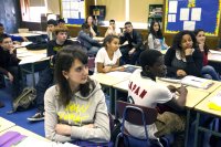 A classroom full of diverse high school students sitting at their desks, looking toward the front of the room