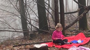 Elementary student sitting on a blanket in the woods reading