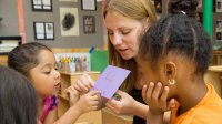 A teacher shows young students a purple construction paper card with the number 4 on it