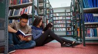 Two high school students reading books in library