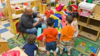 Preschool teacher playing with building blocks with a group of students