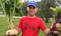 Student holding harvested vegetables while participating in a gardening project through Cabot Leads program.