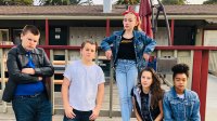 A group of five students wearing greaser outfits, posing outside of their school