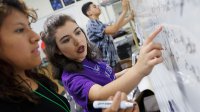 Two high school students work on a math problem together at the class whiteboard