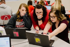 A teacher helping her students with a coding project on their laptops