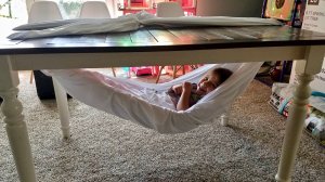 A child lies in a hammock under a table.