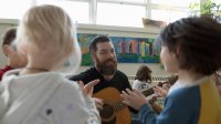 A teacher playing guitar for young elementary students