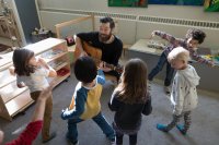 Elementary school teacher playing guitar while children dance around 