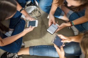 Teenage girls sitting on the floor using cell phones