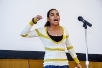 A teenage girl performing spoken word poetry in front of a microphone in a school assembly room