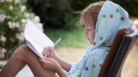 Girl sits outside in summer and writes on paper