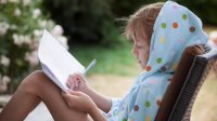 Girl sits outside in summer and writes on paper 