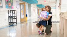 Teacher kneels down to embrace a hug from a young student