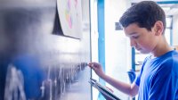 Middle grade aged boy doing a math problem on a chalkboard in school classroom