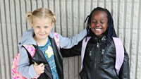 Two elementary school girls are smiling and standing side by side.