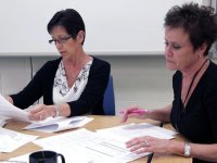 Two teachers working side-by-side at a table covered with papers