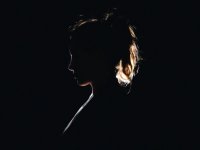 A side profile, silhouette of a young woman with a ponytail, her head slightly tilted down. 