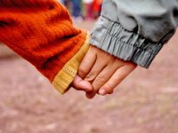 A closeup of two kids holding hands.