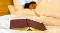 photo of a person sleeping on a bed with an overturned book in the foreground