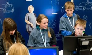 Two girls and two boys at a table with computers against a blue backdrop with city icons