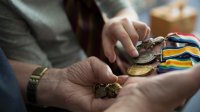 Hands of a student and of a teacher hold several war medals. 