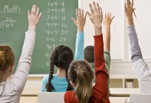 Several students—both female and male—earnestly raise their hands in a classroom.