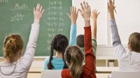 Several students—both female and male—earnestly raise their hands in a classroom.