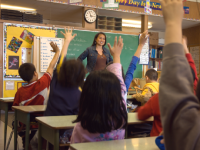 Teacher standing in front of class with students' hands raised