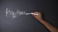 Musical notes flow across a blackboard from a piece of chalk held by a student.