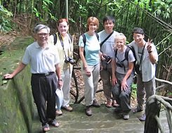 Six people standing together on a bridge, five wearing backpacks and cameras