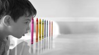 A young boy in black and white sees a colorful collection of crayons. 