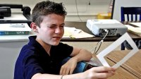 Boy squinting, holding and looking through a cutout in a cardboard frame