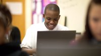 A high school student smiles confidently as he uses his computer. 