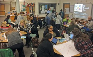 A group of educators are sitting at classroom tables collaborating. 