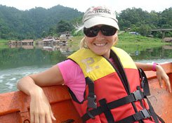 Woman wearing a baseball cap, sun glasses, and a life vest sitting, leaning back in a boat